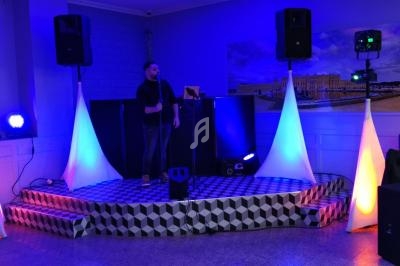 Un homme chante sur une petite scène éclairée par des lumières colorées dans une salle de réception.