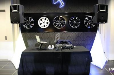 Table de mixage avec ordinateur portable et casque, entourée de haut-parleurs, devant un mur décoré de jantes.