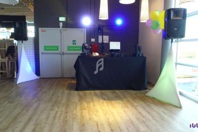 Table de mixage avec équipement audio et éclairage coloré dans une salle au sol en bois, décorée de ballons.