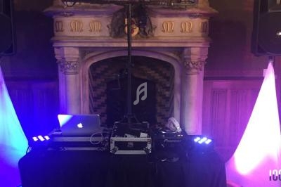 Installation de DJ avec platines, ordinateur et éclairages colorés devant une cheminée décorative.