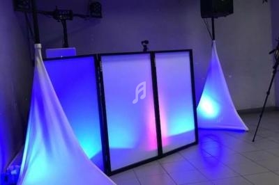 Console de DJ éclairée par des lumières colorées dans une salle avec des haut-parleurs et des décorations suspendues.