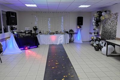 Salle décorée pour une fête avec table de buffet, piste noire parsemée de pétales et ballons en arrière-plan.