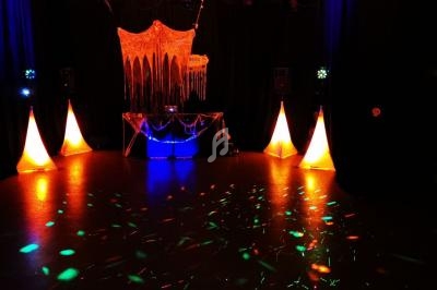 Salle sombre décorée pour une fête, avec lumières colorées, guirlandes et une table ornée d'un tissu suspendu.