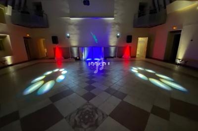 Salle de réception avec éclairage coloré, projecteurs au sol et une console de DJ illuminée au centre.