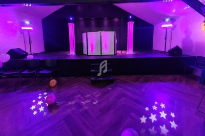 Scène éclairée de lumières violettes avec une piste de danse en parquet et des ballons au sol.