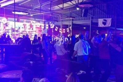 Groupe de personnes dans une ambiance festive avec éclairage coloré, près d'un bar et d'une piste de danse.