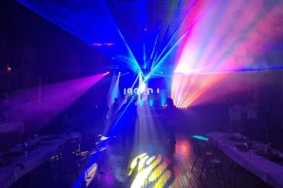 Salle sombre illuminée par des faisceaux lumineux colorés, avec des silhouettes de personnes en arrière-plan.