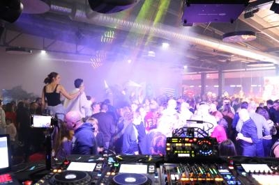 Vue d'une piste de danse animée dans une salle, avec des personnes dansant sous des jeux de lumière colorés.