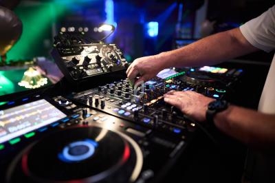 Main d'un DJ ajustant les commandes d'une table de mixage dans un environnement lumineux de soirée.