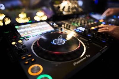 Platines DJ avec des boutons lumineux et un écran affichant des pistes audio, utilisées lors d'une performance musicale.