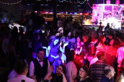 Groupe de personnes dans une ambiance festive, éclairées par des lumières colorées dans un bar ou une discothèque.
