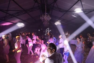 Des personnes dansent sous des jeux de lumière dans une grande salle avec un plafond en structure métallique.