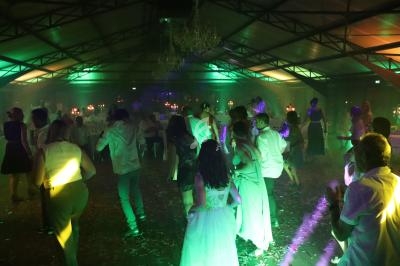 Des personnes dansent dans une salle éclairée par des lumières colorées, avec un plafond métallique et un lustre central.