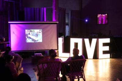 Un couple assis regarde une projection de photos dans une salle décorée avec des lettres lumineuses formant ’LOVE’.