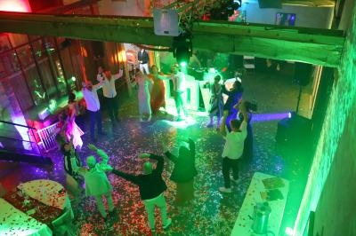 Personnes dansant sous des lumières colorées dans une salle décorée, avec confettis au sol.