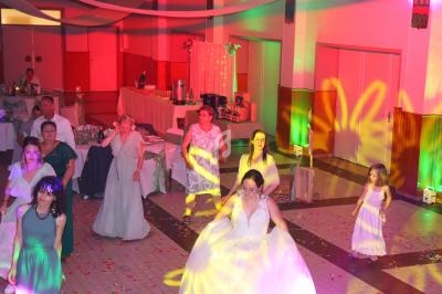 Des invités dansent dans une salle décorée, éclairée par des lumières colorées lors d'une fête ou d'un mariage.