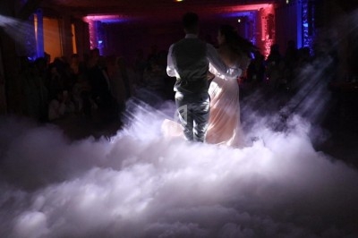 Un couple danse au milieu d'une piste enveloppée de fumée, éclairée par des lumières colorées.