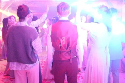 Des personnes dansent sous des lumières colorées dans une ambiance festive, avec des confettis au sol.