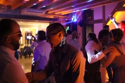 Des personnes dansent et discutent dans une salle éclairée par des lumières colorées lors d'un événement festif.