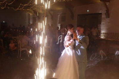 Un couple danse lors de leur mariage dans une salle décorée, avec des étincelles lumineuses en premier plan.