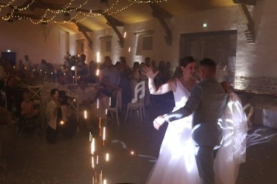 Un couple danse sous des lumières scintillantes dans une salle décorée pour une réception avec des invités en arrière-plan.