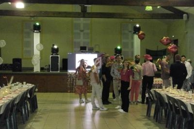 Des personnes déguisées discutent dans une salle décorée pour une fête, avec tables dressées et une scène en arrière-plan.