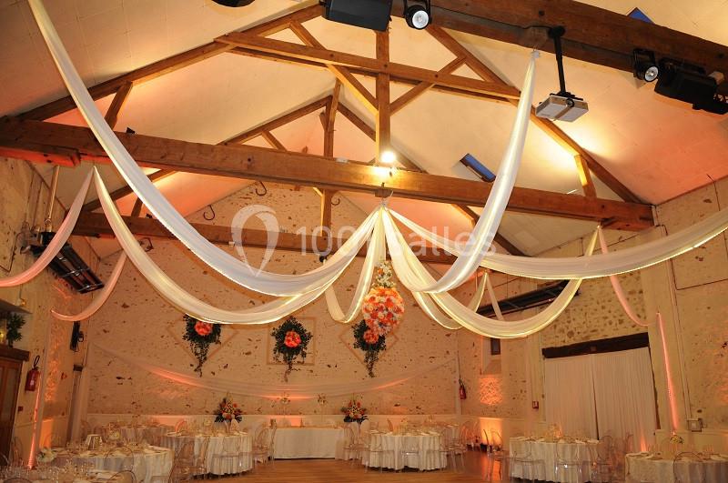 Salle de réception décorée avec des drapés blancs suspendus, des fleurs et des tables dressées pour un événement.