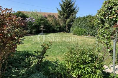 Terrain de sport en plein air avec pelouse et piste en terre, entouré de maisons et d'arbres sous un ciel dégagé.