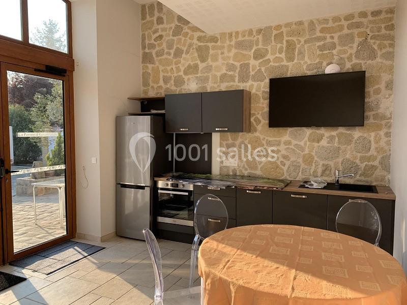 Cuisine moderne avec mur en pierre, meubles noirs, réfrigérateur, table ronde avec nappe orange et grande porte vitrée.