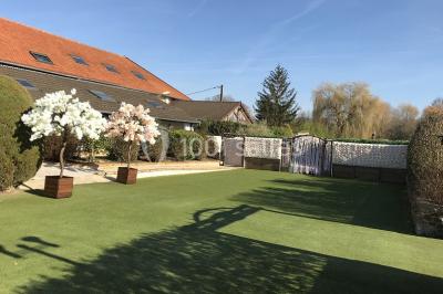 Terrain de sport en plein air avec pelouse et piste en terre, entouré de maisons et d'arbres sous un ciel dégagé.