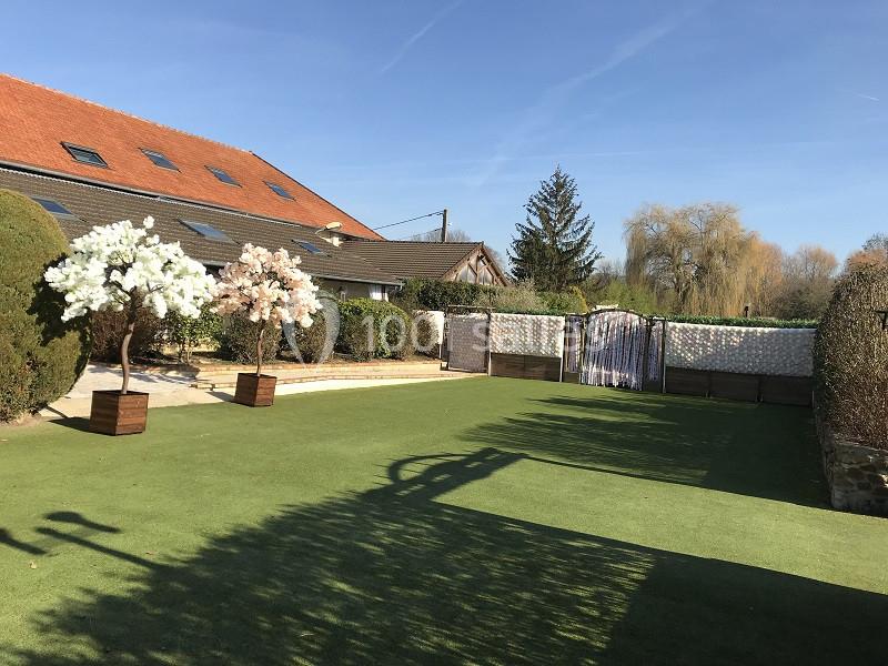 Cour extérieure avec pelouse artificielle, arbres décoratifs en pots, clôture en bois et mur végétalisé.