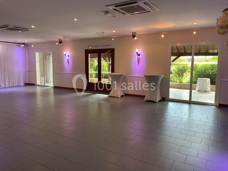 Salle vide avec sol carrelé, murs clairs, éclairage doux, tables hautes et vue sur un espace extérieur verdoyant.