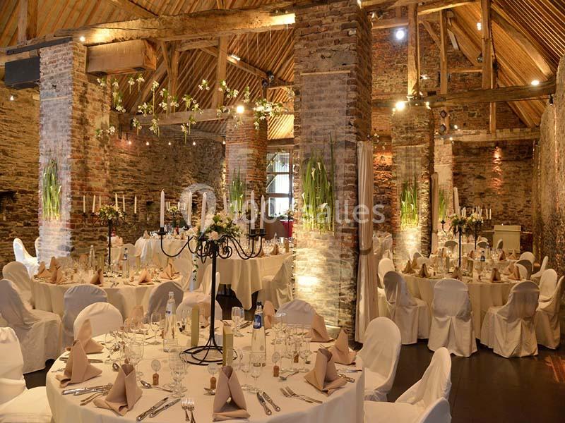 Salle de réception rustique avec murs en briques, poutres apparentes et tables décorées pour un événement festif.