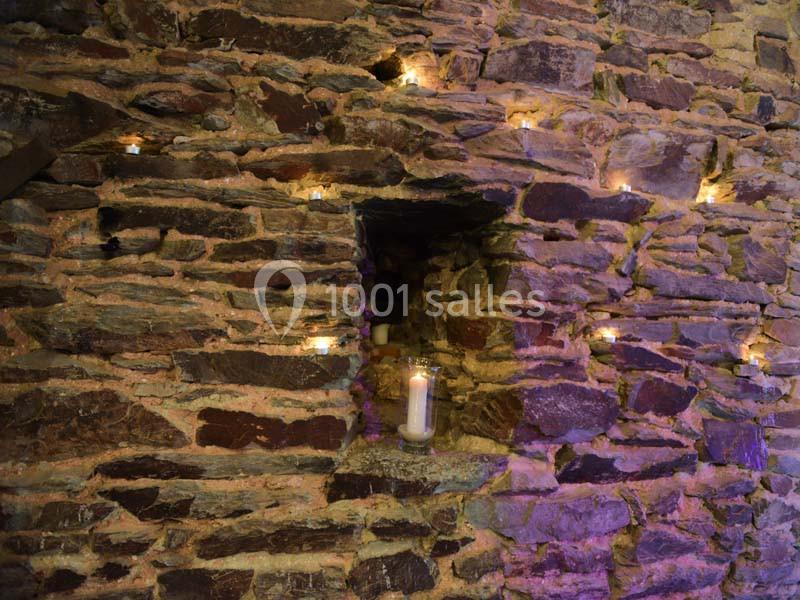 Mur en pierre éclairé par des bougies, avec une niche centrale contenant une bougie allumée.