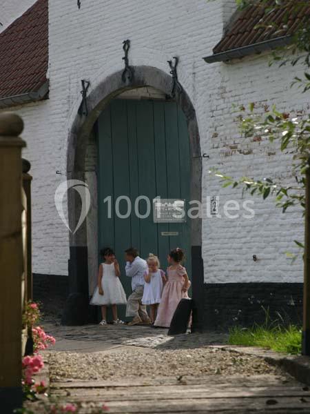Des enfants en tenue élégante entrent par une grande porte en bois vert d'un bâtiment blanc ancien.