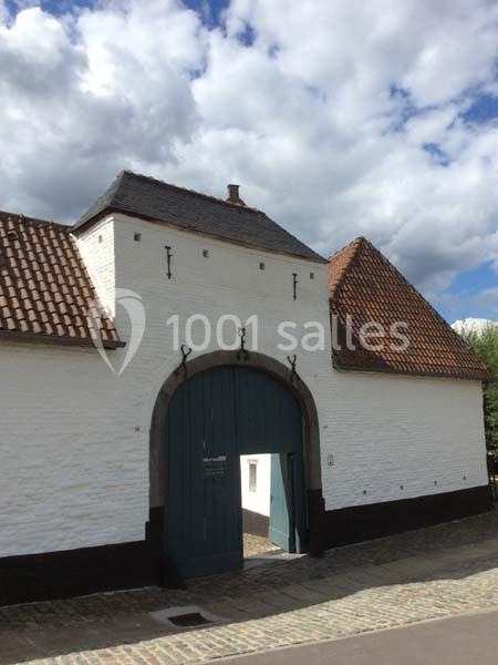 Façade d'un bâtiment ancien en briques blanches avec une grande porte cochère en bois vert et un toit en tuiles.