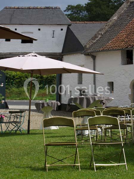 Chaises pliantes disposées sur une pelouse devant des tables et des parasols, près de bâtiments en pierre blanche.