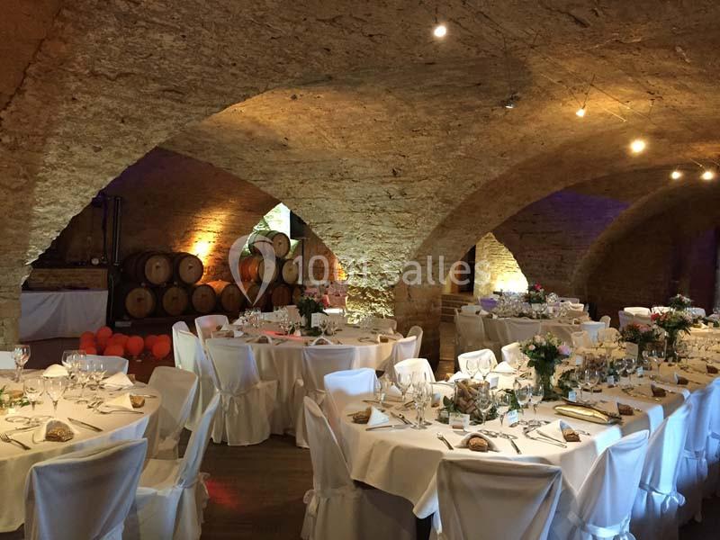 Salle voûtée en pierre aménagée pour un banquet, avec tables dressées, nappes blanches et décorations florales.