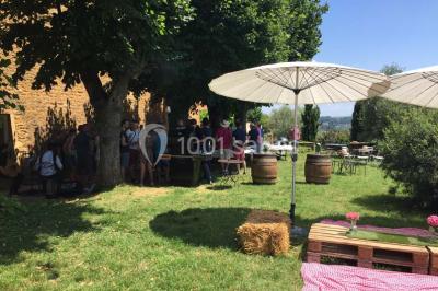 Bouteille de vin rouge posée sur une surface en pierre, avec des fleurs floues et un paysage en arrière-plan.