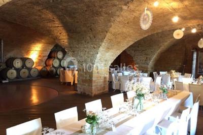 Bouteille de vin rouge posée sur une surface en pierre, avec des fleurs floues et un paysage en arrière-plan.