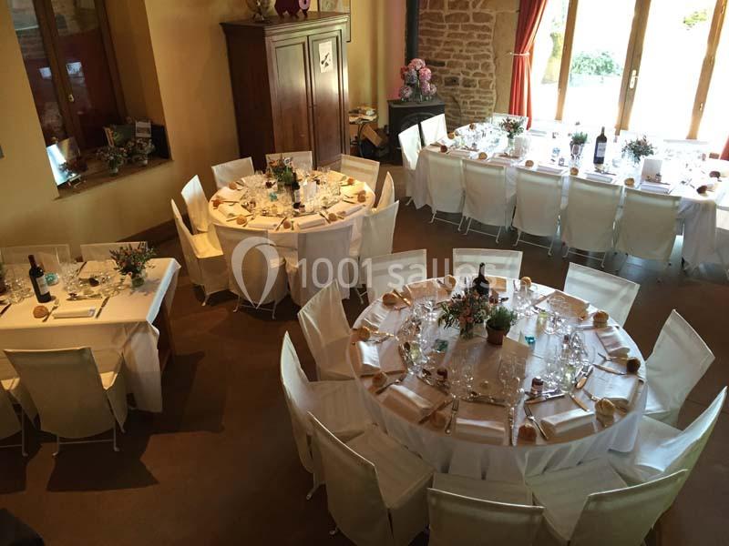 Salle de réception avec tables rondes et rectangulaires dressées, décorées de fleurs et nappes blanches.