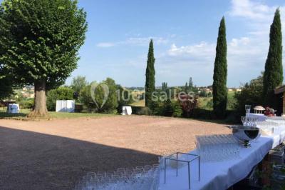 Bouteille de vin rouge posée sur une surface en pierre, avec des fleurs floues et un paysage en arrière-plan.