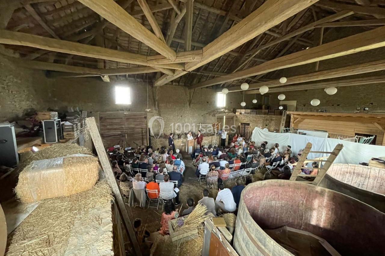 Un groupe de personnes assises dans une grange en bois, assistent à une présentation ou un spectacle.