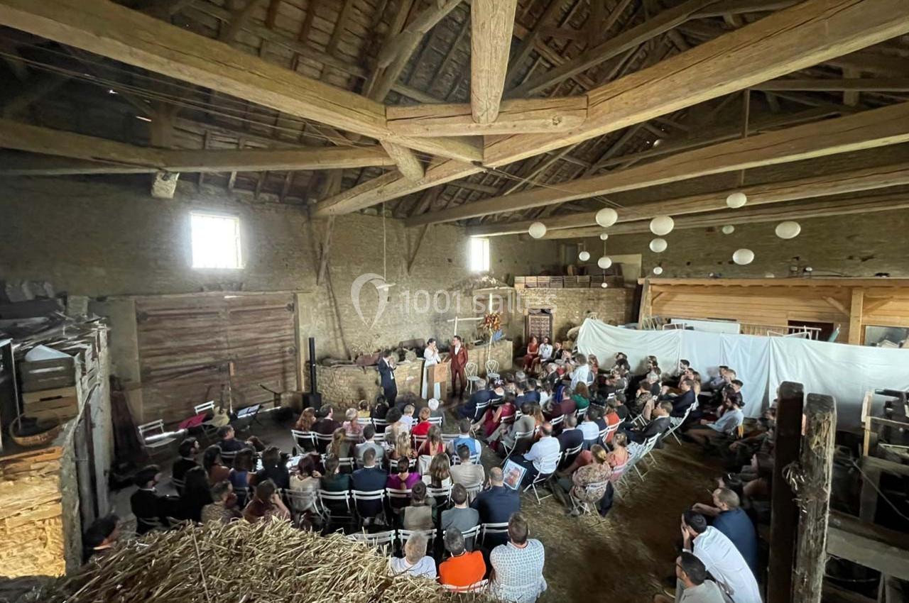 Un groupe de personnes assiste à une représentation dans une grange rustique avec des bottes de foin et des poutres…