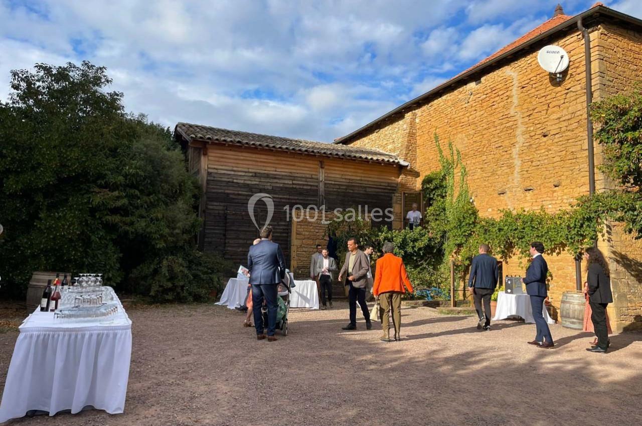 Personnes discutant dans une cour extérieure devant un bâtiment en pierre, avec des tables dressées pour un événement.