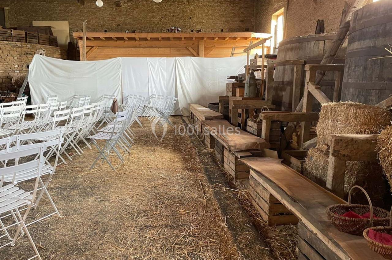Salle rustique aménagée avec des chaises blanches pliantes, des bancs en bois et des éléments de décoration champêtre.