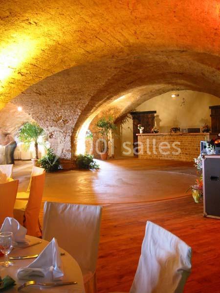 Salle voûtée en pierre avec éclairage chaleureux, tables dressées et espace dégagé près d'un comptoir en briques.