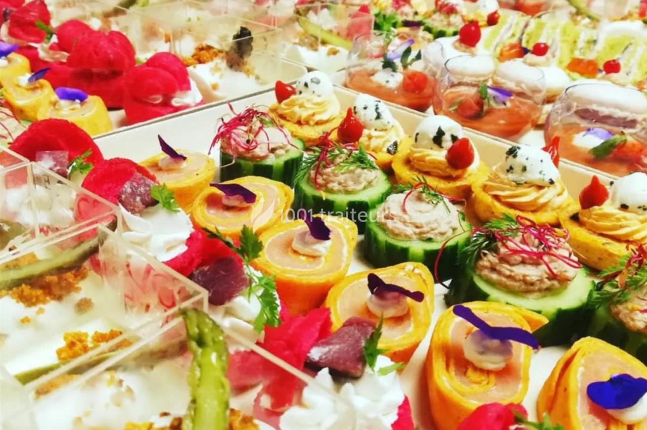 Plateau de bouchées apéritives colorées, composées de légumes, saumon, crèmes et décorations florales.