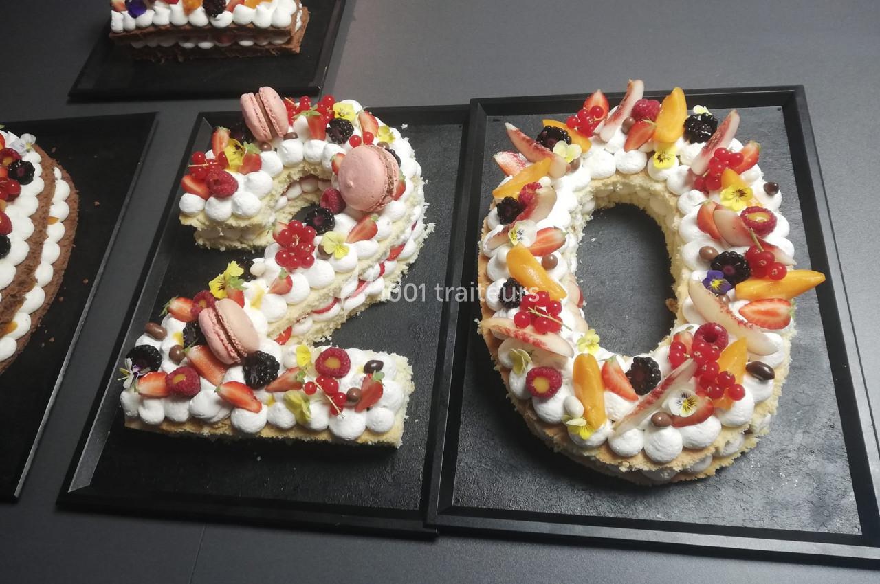 Gâteau en forme du chiffre 20, décoré de fruits frais, macarons et crème, présenté sur un plateau noir.