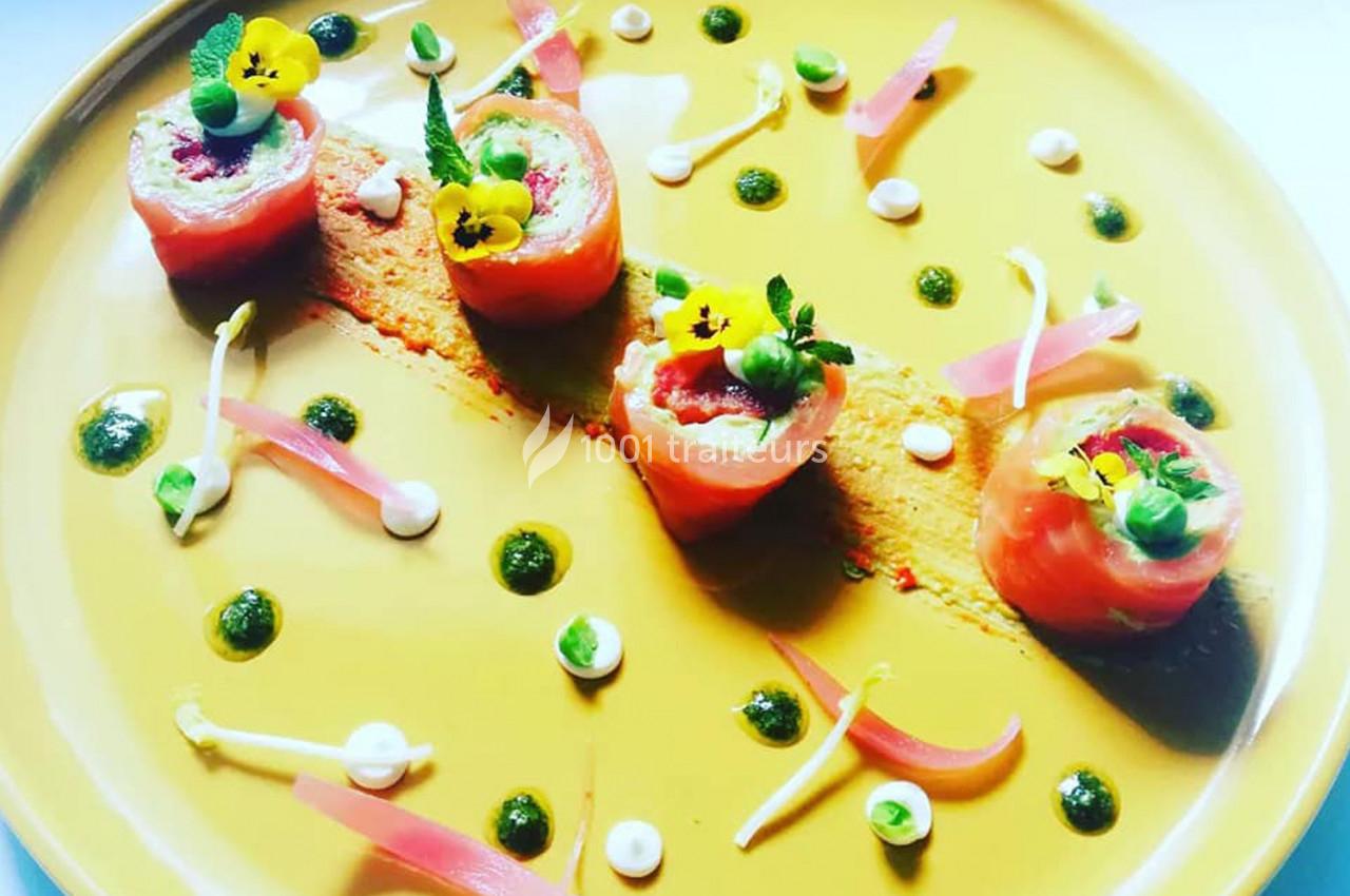 Assiette gastronomique avec roulés de saumon, purée, herbes, fleurs comestibles et décorations colorées.